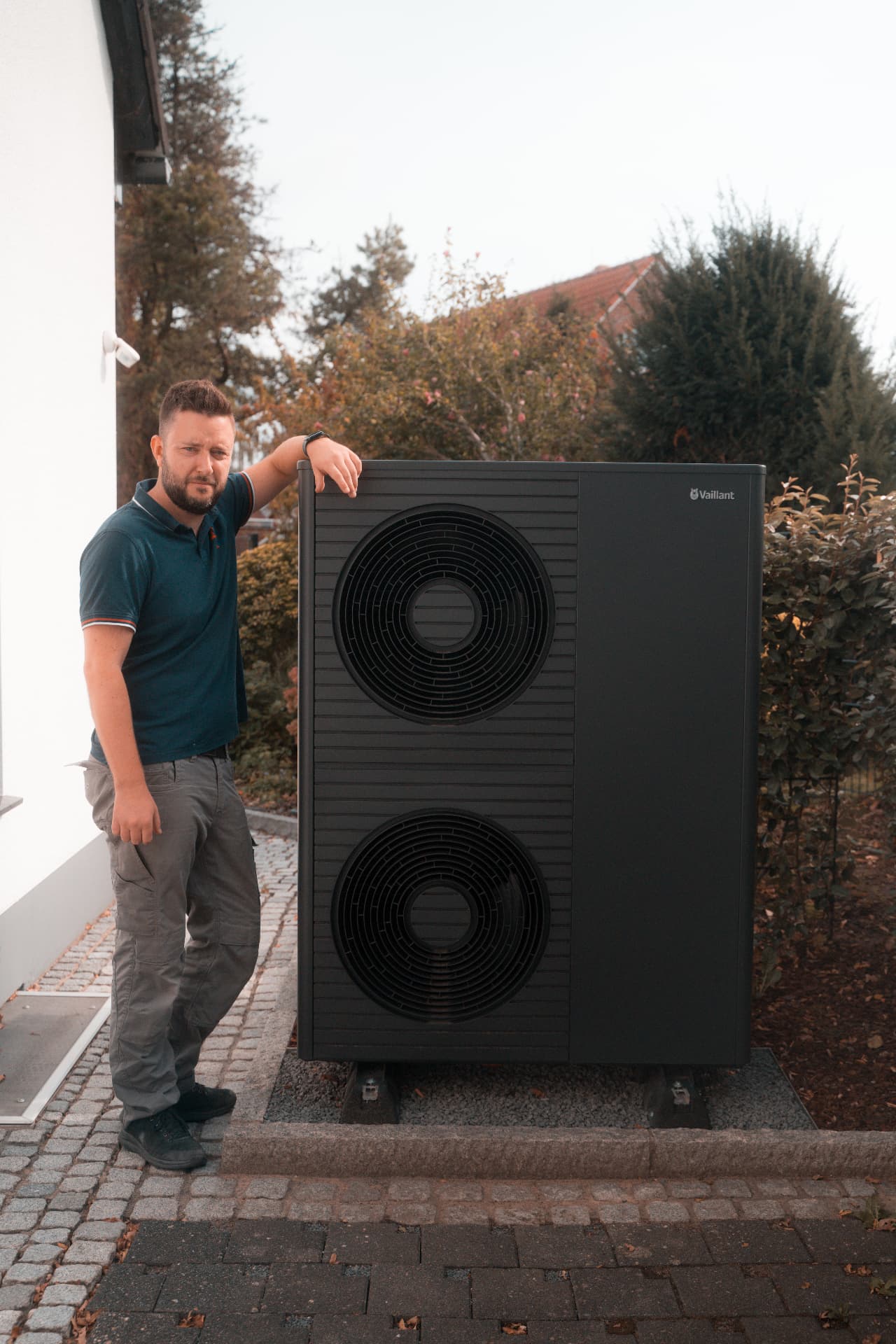 Vaillant Wärmepumpen-Außeneinheit neben einem Einfamilienhaus, daneben ein Monteur von HeissKalt